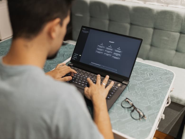 Una persona, vista de espaldas, escribe una consulta a un asistente de inteligencia artificial abierto en la pantalla de su computadora portátil.